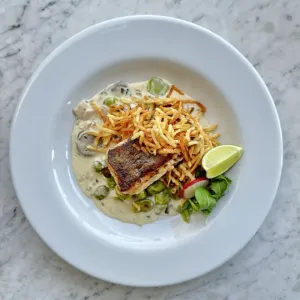 Merluza austral sobre salsa a base de crema, habas, jamón y champiñones